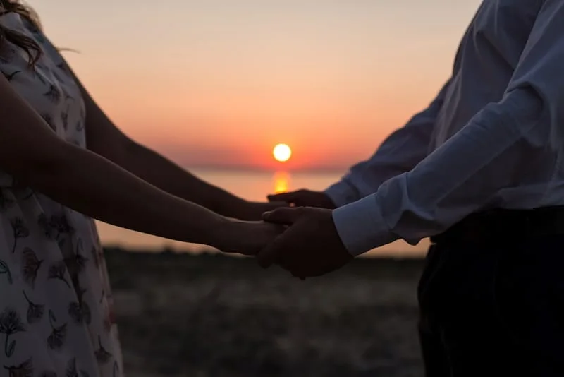 Dos manos entrelazadas a contraluz durante un atardecer